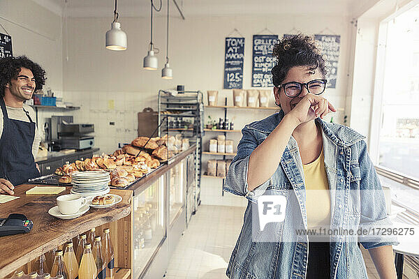 Männlicher Besitzer schaut auf fröhliche weibliche Kundin im Café