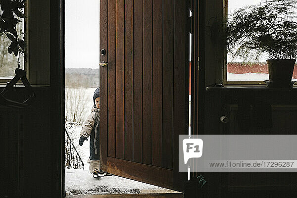 Full length of girl standing behind door during winter