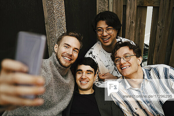 Smiling multi-ethnic male friends taking selfie on mobile phone in balcony