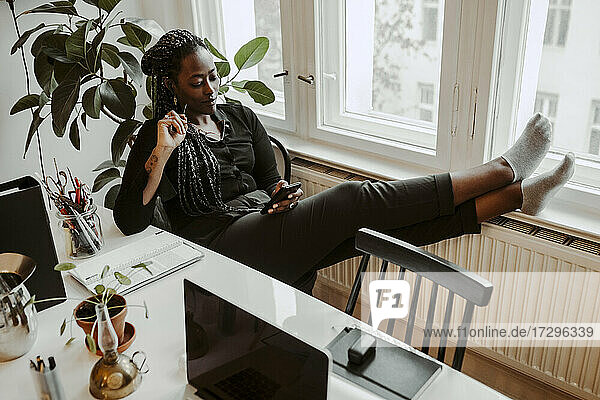 Junge Geschäftsfrau Text-Messaging durch Smartphone  während in Home-Office sitzen