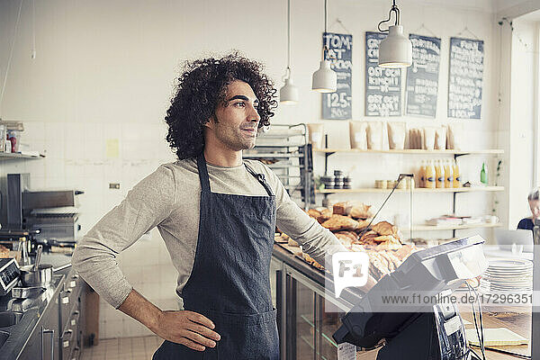 Männlicher Besitzer stehend mit Hand auf der Hüfte an der Kasse in einem Cafe