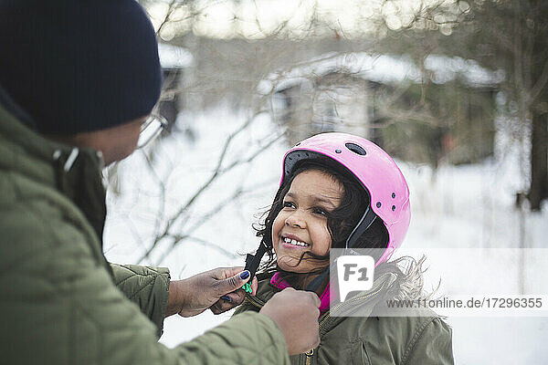 Lächelndes Mädchen schaut auf Mutter Hilfe beim Tragen Helm während des Urlaubs