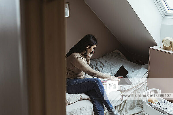 Weiblicher Profi  der ein digitales Tablet benutzt  während er mit einem Smartphone im Schlafzimmer spricht
