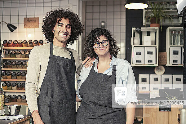 Portrait of smiling male and female entrepreneurs wearing apron standing at organic shop