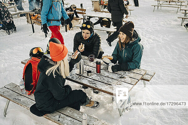 Männliche und weibliche Freunde reden beim Essen Hot Dog im Skigebiet im Winter