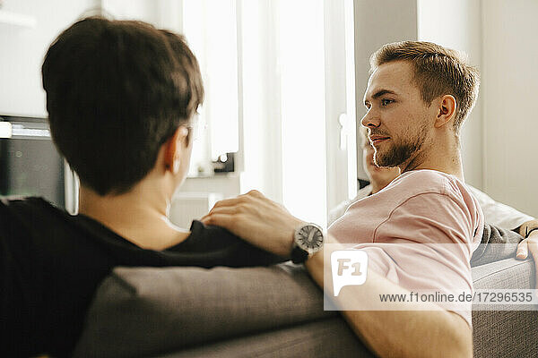 Young man talking with male friends while sitting at home