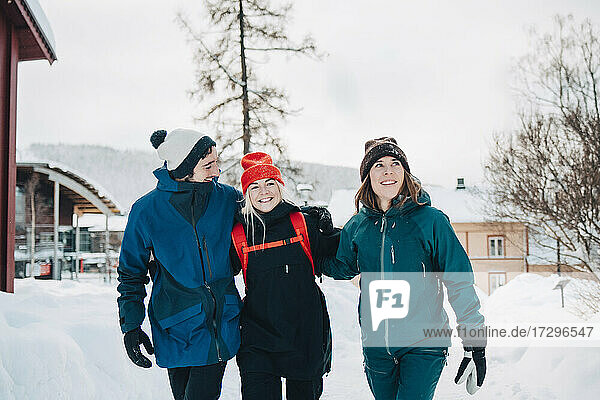 Cheerful male and female friends walking with arm around at ski resort