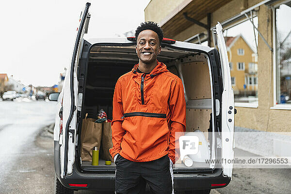 Portrait of smiling essential service man standing with hands in pockets against delivery van