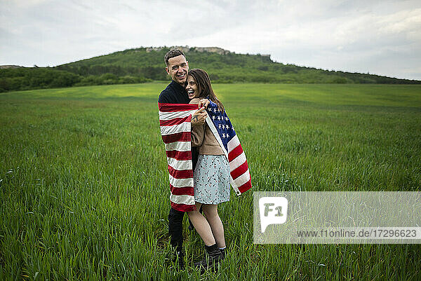 Lächelndes junges Paar in amerikanischer Flagge eingewickelt in einem Weizenfeld