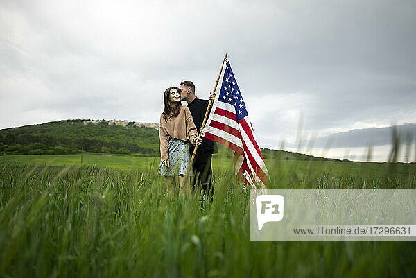 Junges Paar mit amerikanischer Flagge  das sich in einem Weizenfeld küsst