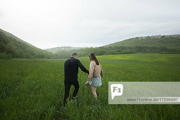 Rear view of young couple walking in wheat field in rain