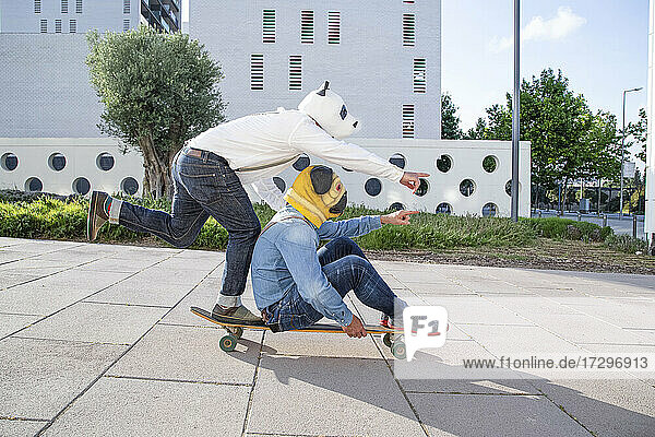 Two men with animal mask on longboard in park