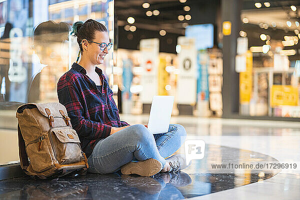 Spanish woman smiling and sitting looking at laptop in shopping mall