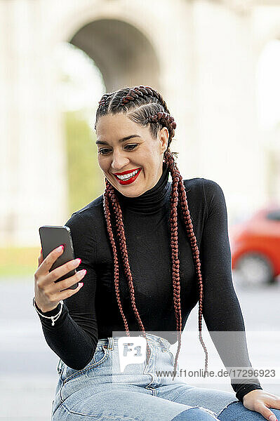 Schöne Frau mit Zöpfen  die ein Mobiltelefon benutzt und lächelt