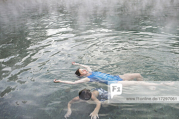 Eine Mutter und ihr Sohn schwimmen im Pool von Trinity Hot Springs  aus dem Dampf aufsteigt
