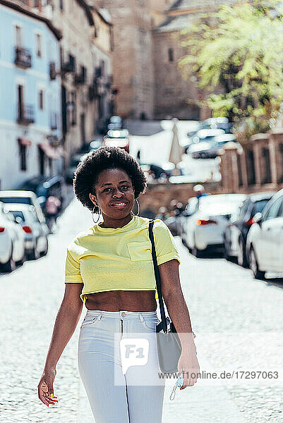 Schwarzes Mädchen mit Afro-Haar  das fröhlich eine Stadtstraße entlangläuft.