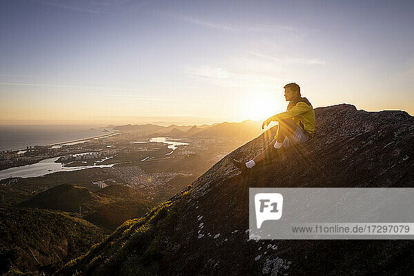 Mann sitzt auf felsigen Bergkante mit schönen Sonnenuntergang Landschaft