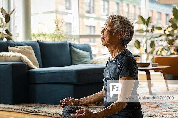 Asiatische ältere Frau meditiert und entspannt zu Hause im Wohnzimmer