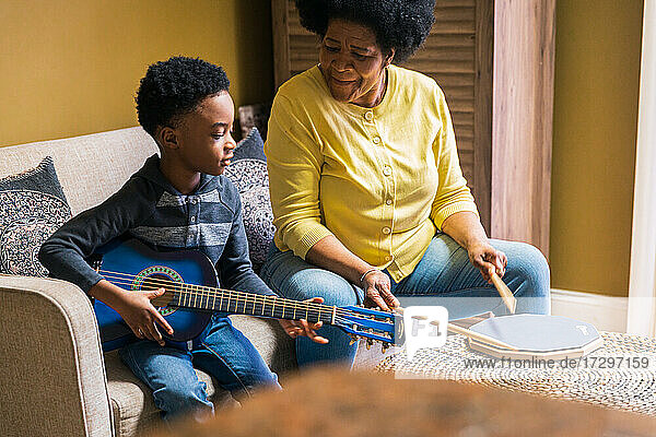 Senior woman playing drum pad while grandson playing guitar at home