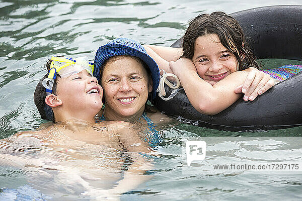 Eine Mutter umarmt ihre beiden Kinder im Vorschulalter  während sie im Pool schwimmt.
