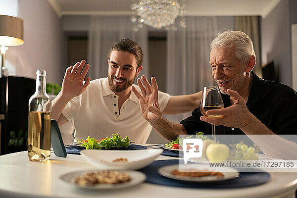 Großvater und Enkel im Gespräch mit Online-Verwandten beim Abendessen