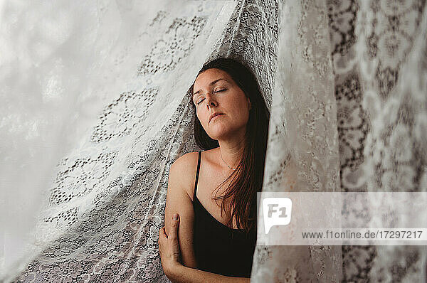 Beautiful woman with long brown hair surrounded by lace curtains.
