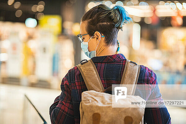 Back of Spanish woman with mask glasses and backpack shopping in mall