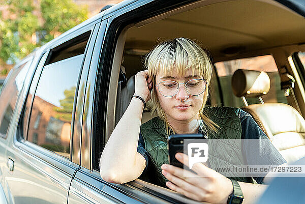 Teenager sitting in passenger seat of car looking at cell phone