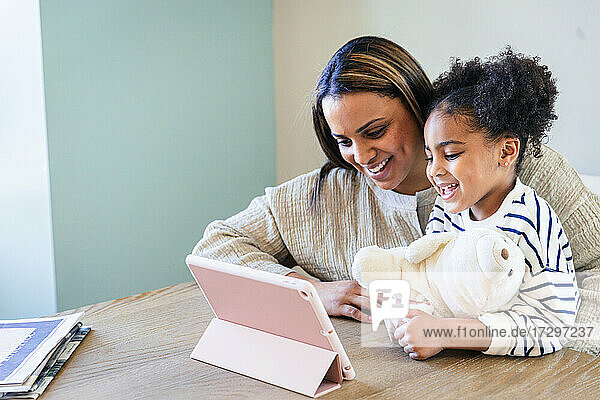 Smiling daughter and mother using digital tablet at home