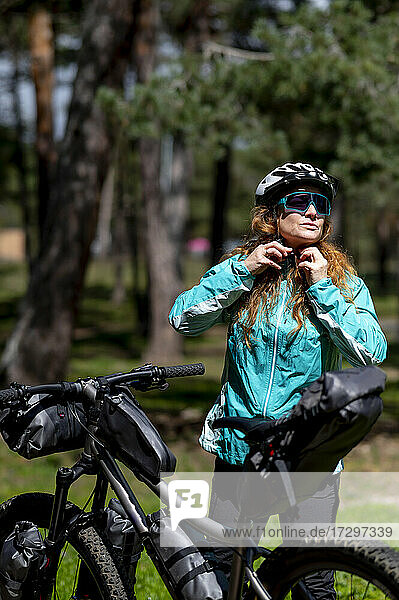 Eine Frau neben ihrem Mountainbike  die ihren Schutzhelm befestigt