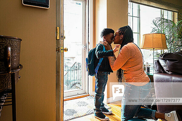 Mutter küsst Sohn  der zur Schule geht  am Eingang des Hauses