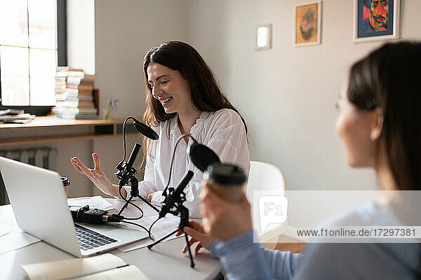 Glückliche Frau lächelt und spricht in ein Mikrofon während eines Podcasts mit einem Freund