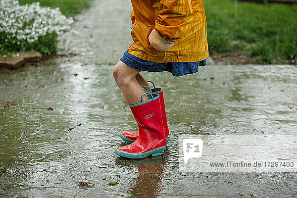 A small child in bright rain boots plays in the pouring rain outside