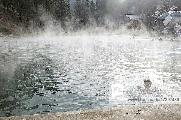 A boy jumps into a Trinity Hot Springs pool with steam rising from it.