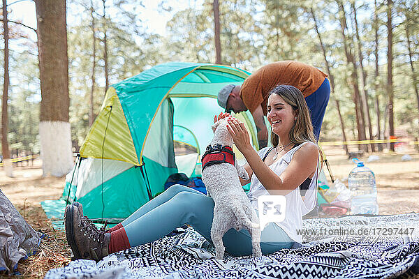 Glückliches junges Paar mit Hund vor dem Zelt sitzend
