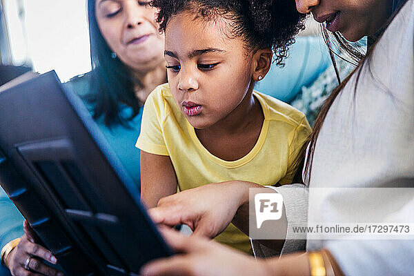 Niedliches Mädchen  das sich ein Fotoalbum ansieht  während es mit seiner Familie zu Hause sitzt