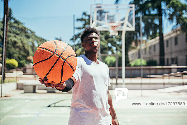 Porträt eines afroamerikanischen schwarzen Jungen  der den Basketball auf einem städtischen Basketballplatz hält.