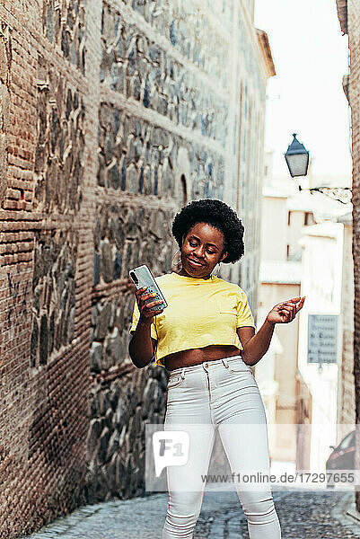 Porträt eines schwarzen afro-amerikanischen Mädchens  das ihr Handy benutzt und auf einer Straße in der Altstadt tanzt.