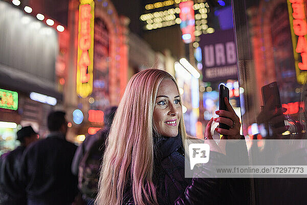 Frau mit Smartphone auf nächtlich leuchtender zentraler Straße