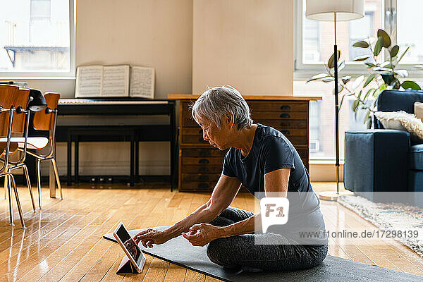 Ältere Frau benutzt ein digitales Tablet  während sie im Wohnzimmer trainiert