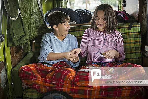 Brother and sister play cards in back of VW camper van during roadtrip