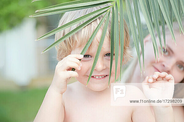 Glücklicher Junge spielt mit grünem Palmzweig im Sommer
