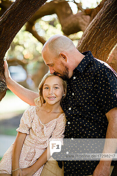 Vater küsst junge Tochter auf den Kopf in einem Baum in San Diego
