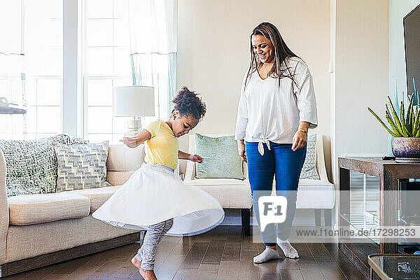 Lächelnde Mutter  die ihre Tochter beim Tanzen im heimischen Wohnzimmer beobachtet