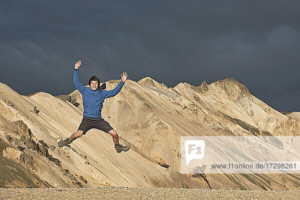Jugendlicher springt vor den Bergen von Landmannalaugar / Island