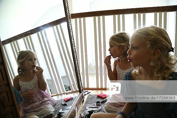 zwei kleine Mädchen schauen in den Spiegel und tragen Lippenstift auf