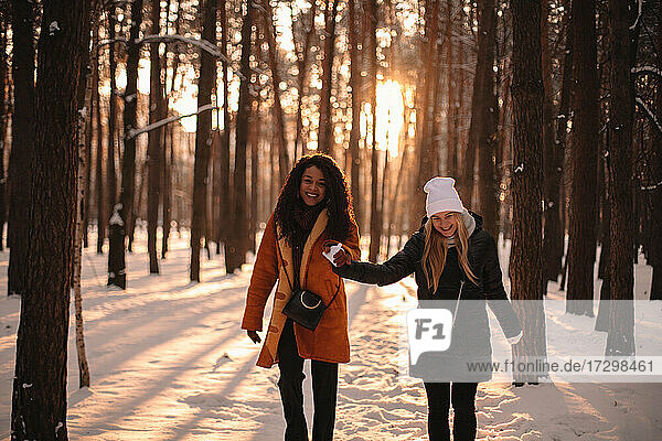 Happy girlfriends holding hands while walking in snow covered park