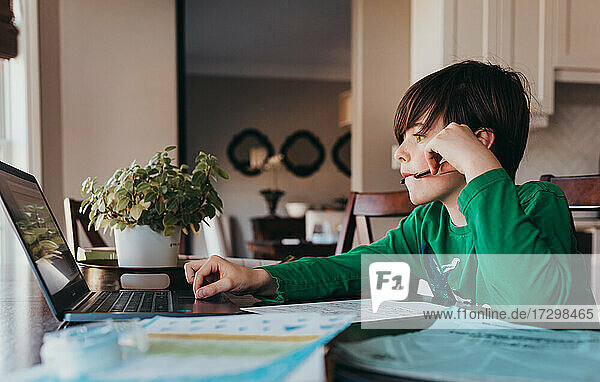 Junger Junge  der am Computer am Küchentisch online Schularbeiten erledigt.