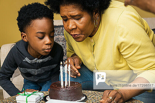 Großmutter und Enkel blasen zu Hause Kerzen auf dem Geburtstagskuchen aus