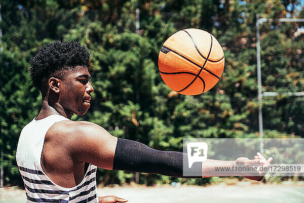 Seitenansicht eines schwarzen afroamerikanischen Jungen  der auf einem städtischen Platz mit einem Basketball spielt.